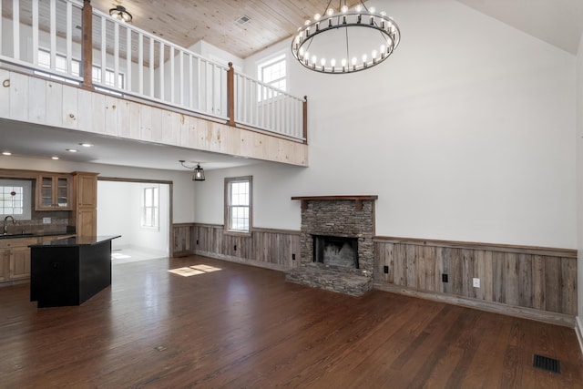 unfurnished living room with dark wood-style floors, a wainscoted wall, visible vents, a fireplace, and a notable chandelier