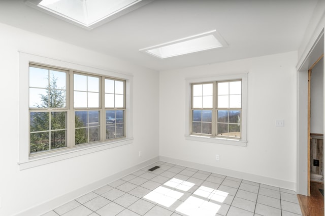 empty room featuring a skylight, light tile patterned floors, and baseboards