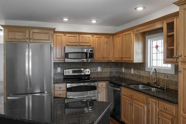 kitchen with backsplash, appliances with stainless steel finishes, dark stone counters, and a sink