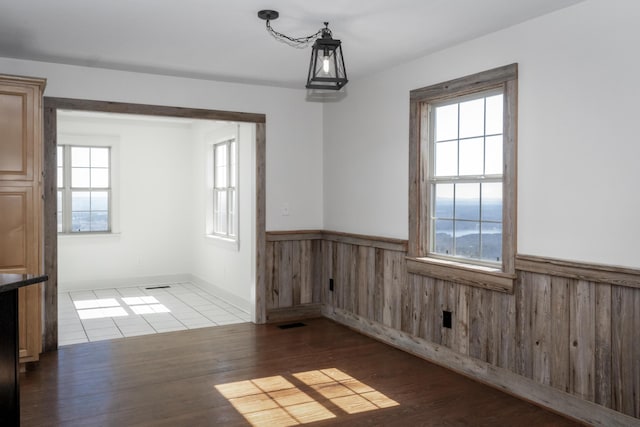 unfurnished dining area featuring visible vents, wood finished floors, a wainscoted wall, and wood walls