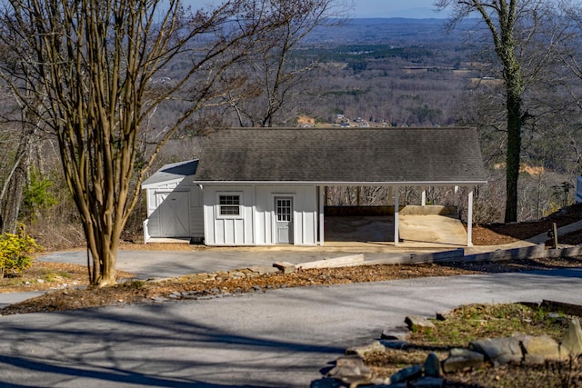 view of shed with an attached carport, driveway, and a forest view