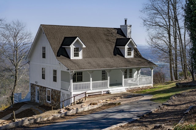 view of front facade with stone siding, a porch, board and batten siding, a shingled roof, and a chimney