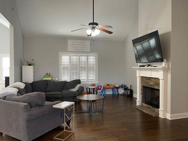 living area with baseboards, a ceiling fan, wood finished floors, a stone fireplace, and high vaulted ceiling