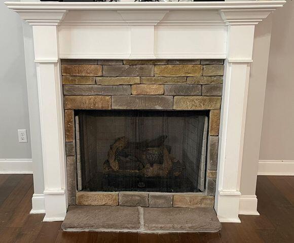 details with a stone fireplace, wood finished floors, and baseboards