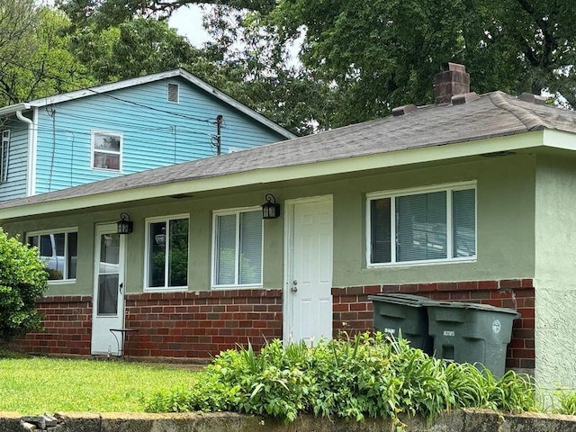 view of front of house with roof with shingles, a chimney, a porch, and brick siding