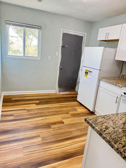 kitchen with baseboards, white cabinets, dark stone countertops, freestanding refrigerator, and light wood-type flooring