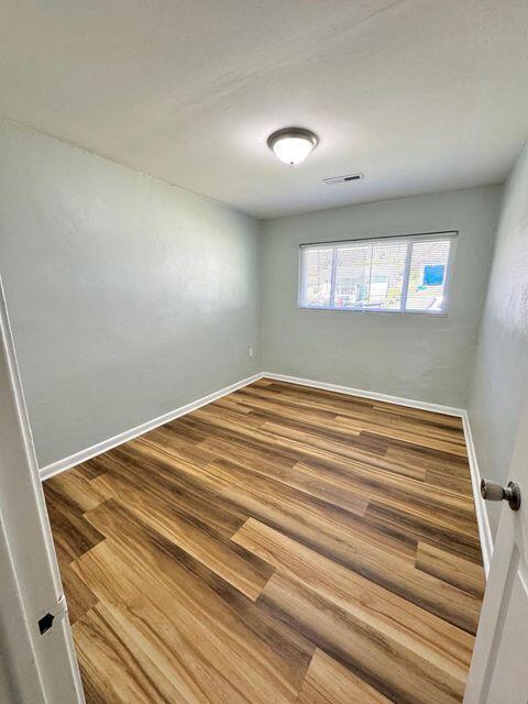 empty room featuring wood finished floors, visible vents, and baseboards