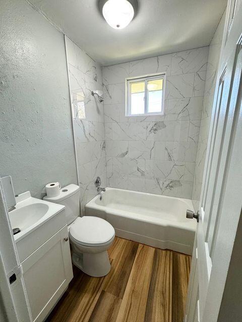 full bathroom with shower / bathtub combination, a textured wall, toilet, vanity, and wood finished floors