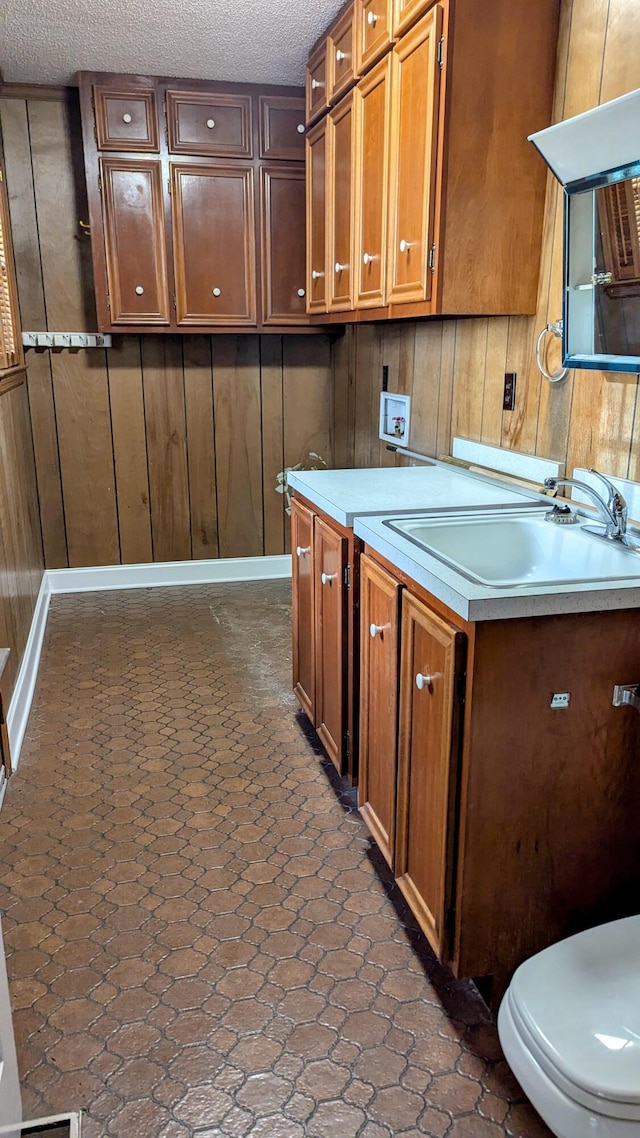 kitchen with brown cabinetry, light countertops, a sink, and wood walls