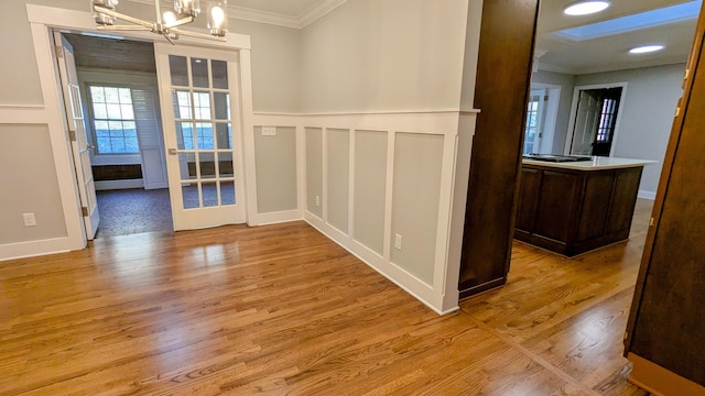 interior space featuring a wainscoted wall, ornamental molding, an inviting chandelier, light wood-type flooring, and a decorative wall