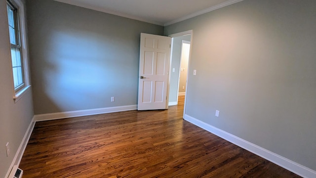 spare room with crown molding, dark wood finished floors, visible vents, and baseboards