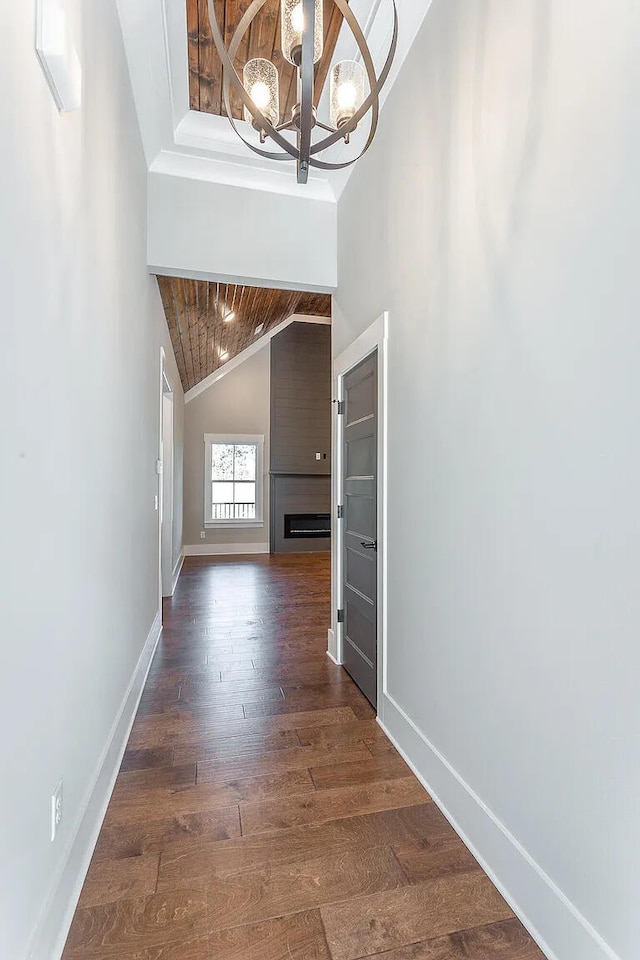 corridor with a notable chandelier, dark wood-type flooring, high vaulted ceiling, wooden ceiling, and baseboards