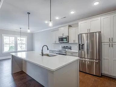 kitchen featuring a sink, white cabinetry, light countertops, appliances with stainless steel finishes, and a center island with sink