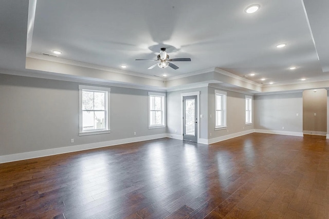 spare room with baseboards, dark wood finished floors, a ceiling fan, ornamental molding, and a tray ceiling