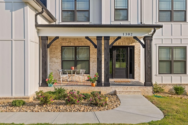 entrance to property featuring board and batten siding, a porch, and brick siding