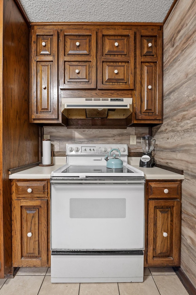 kitchen featuring electric range, brown cabinets, extractor fan, light countertops, and light tile patterned flooring