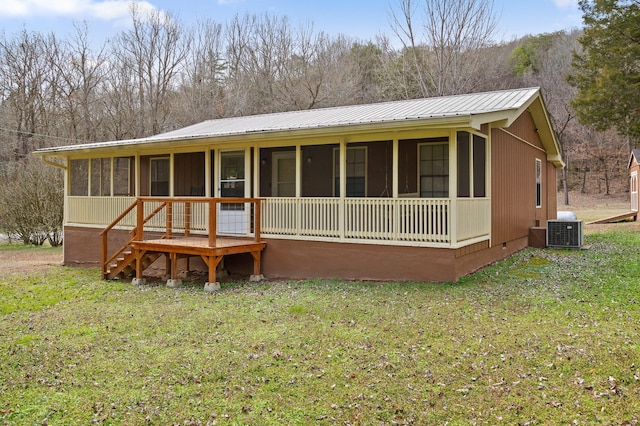 back of property with a sunroom, central AC unit, metal roof, and a yard