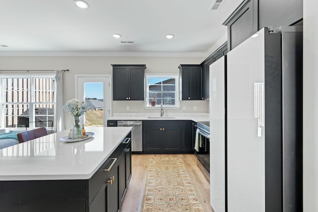 kitchen with stainless steel appliances, visible vents, light wood-style flooring, ornamental molding, and a sink