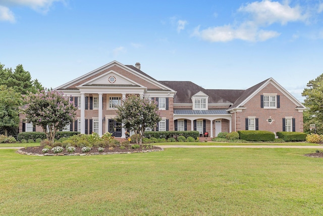 neoclassical home with a front yard, a chimney, and brick siding