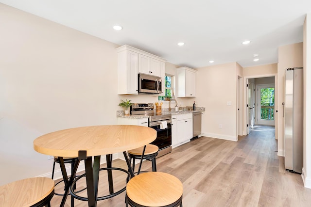 kitchen featuring light wood-style flooring, appliances with stainless steel finishes, white cabinetry, a sink, and baseboards