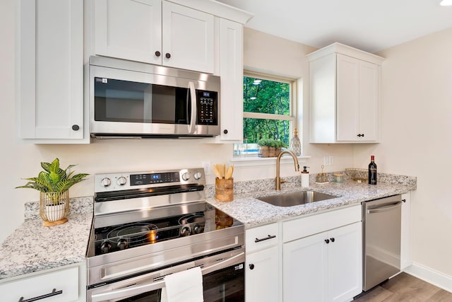 kitchen featuring stainless steel appliances, white cabinetry, a sink, and light stone counters