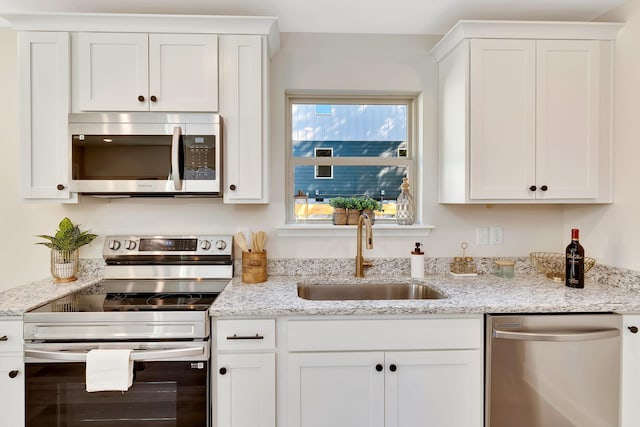 kitchen featuring light stone countertops, white cabinetry, stainless steel appliances, and a sink