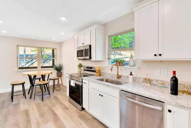 kitchen with stainless steel appliances, light wood-style floors, a sink, and light stone counters