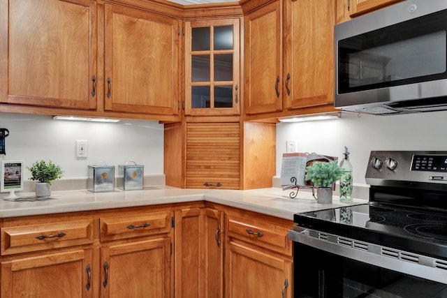 kitchen with glass insert cabinets, brown cabinets, appliances with stainless steel finishes, and light countertops