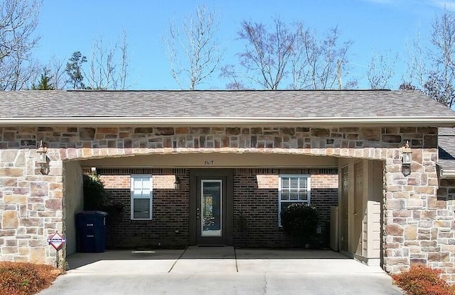 view of exterior entry with an attached carport, stone siding, brick siding, and a shingled roof