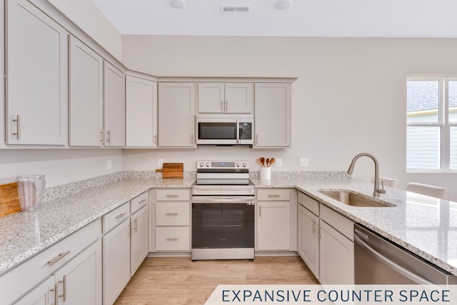 kitchen with light wood-type flooring, visible vents, a sink, stainless steel appliances, and light stone countertops