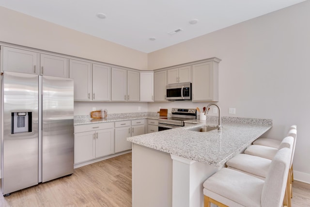 kitchen featuring light stone counters, appliances with stainless steel finishes, a peninsula, light wood-style floors, and a sink