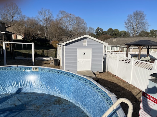 view of pool with a storage unit, an outbuilding, an empty pool, and fence