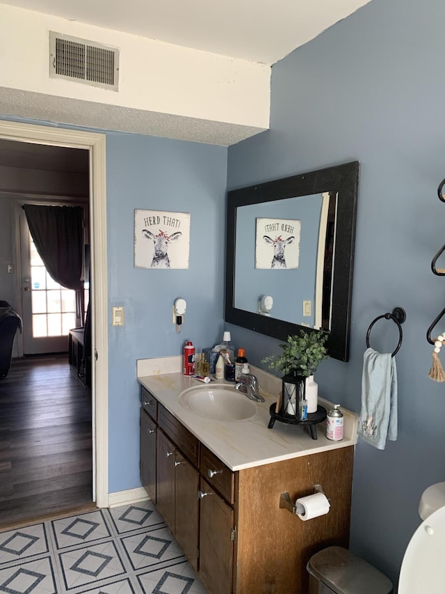 half bath featuring visible vents, baseboards, toilet, and vanity