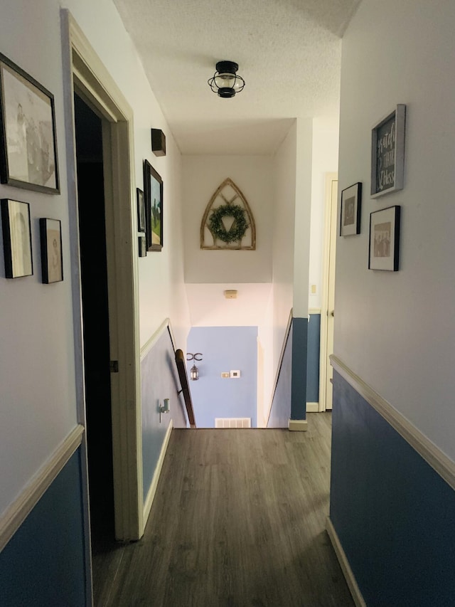 hall with visible vents, dark wood-type flooring, baseboards, an upstairs landing, and a textured ceiling