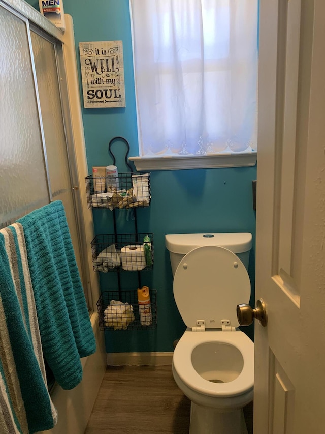 bathroom with an enclosed shower, toilet, baseboards, and wood finished floors