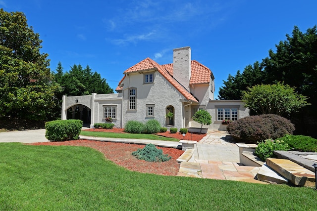 rear view of property with a chimney, a lawn, a tile roof, and stucco siding