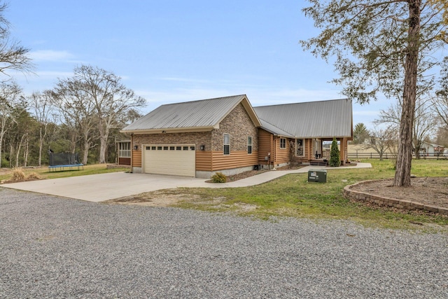 view of front of home with a trampoline, metal roof, a garage, driveway, and a front lawn