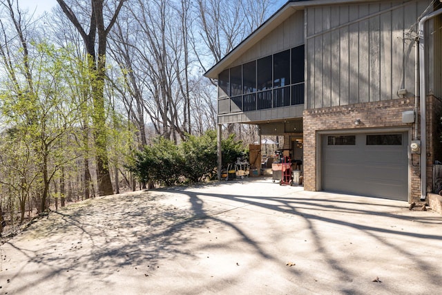 view of property exterior featuring driveway, a sunroom, an attached garage, and brick siding