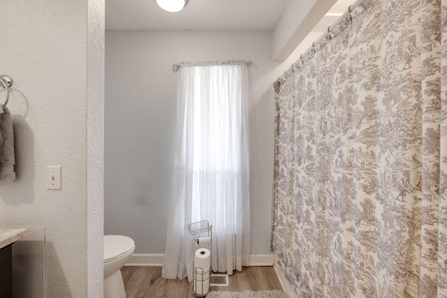 full bath with visible vents, a textured wall, toilet, wood finished floors, and baseboards