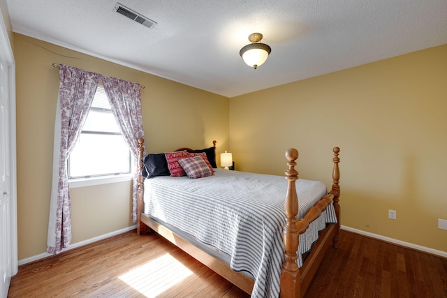 bedroom with a textured ceiling, wood finished floors, visible vents, and baseboards