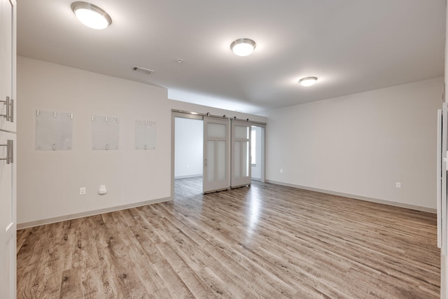 spare room featuring light wood-type flooring, a barn door, visible vents, and baseboards