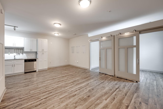 unfurnished living room with light wood-style floors, a barn door, and baseboards