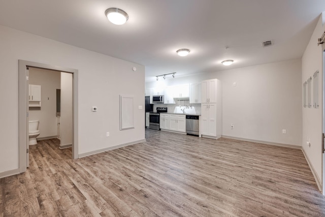 unfurnished living room featuring a sink, light wood-style flooring, visible vents, and baseboards