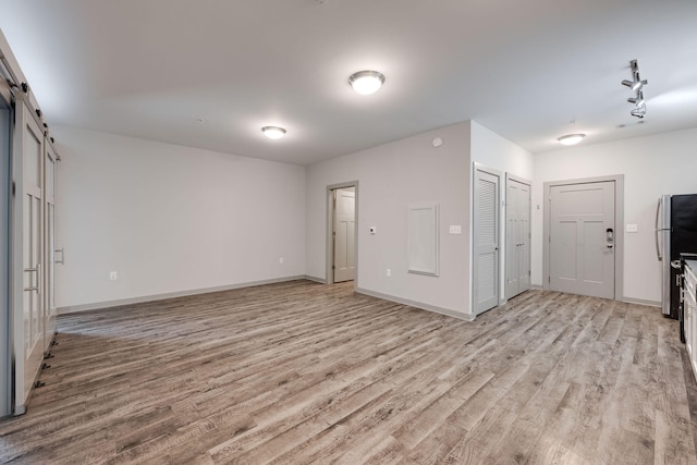 empty room featuring baseboards, a barn door, and light wood-style floors