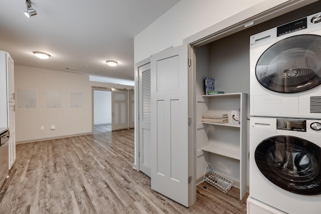 clothes washing area with laundry area, a barn door, baseboards, light wood-style floors, and stacked washing maching and dryer