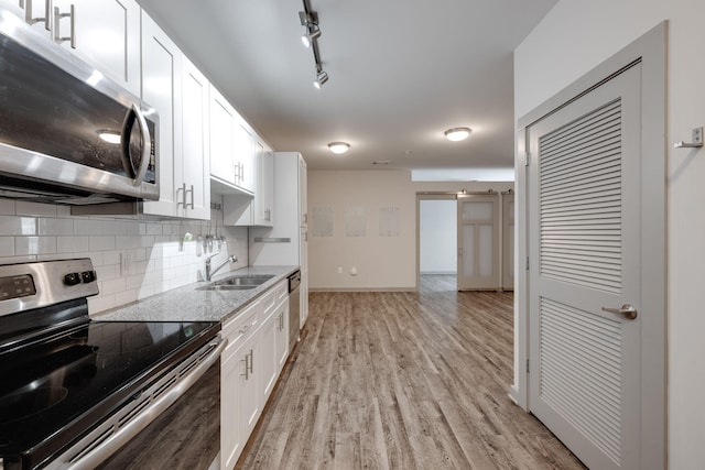 kitchen featuring backsplash, appliances with stainless steel finishes, light wood-style floors, white cabinetry, and a sink