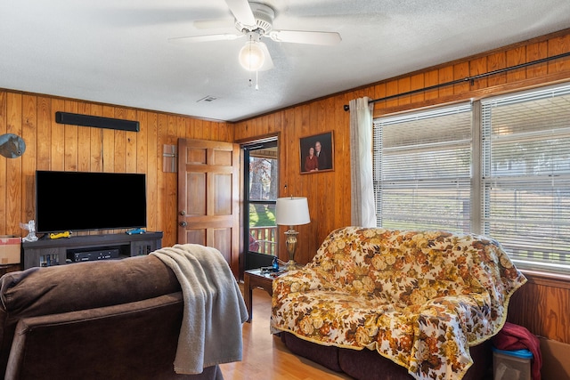 living room featuring ceiling fan, a textured ceiling, wood finished floors, and wooden walls