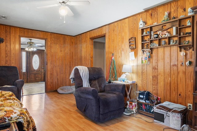 living room featuring light wood-style floors, a ceiling fan, and wood walls