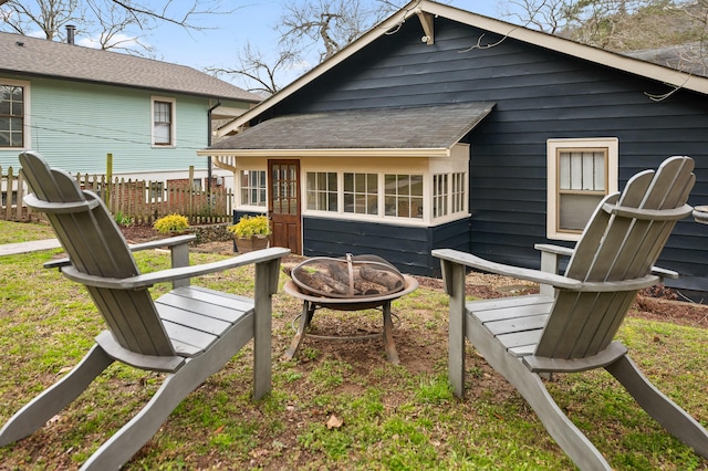 rear view of property with roof with shingles, fence, and a fire pit