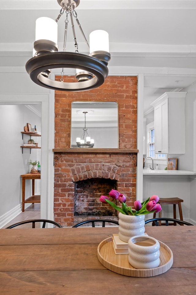 living area with baseboards, a brick fireplace, wood finished floors, and a notable chandelier